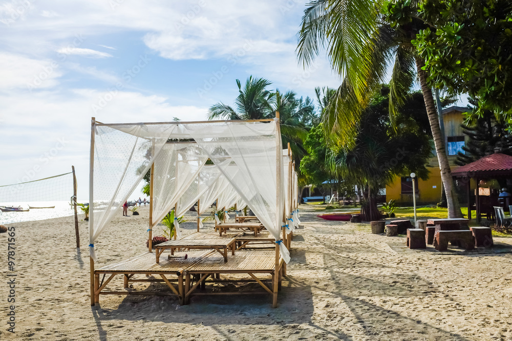 Empty beach bed under thatched umbrellas Empty beach bed under thatched umbrellas