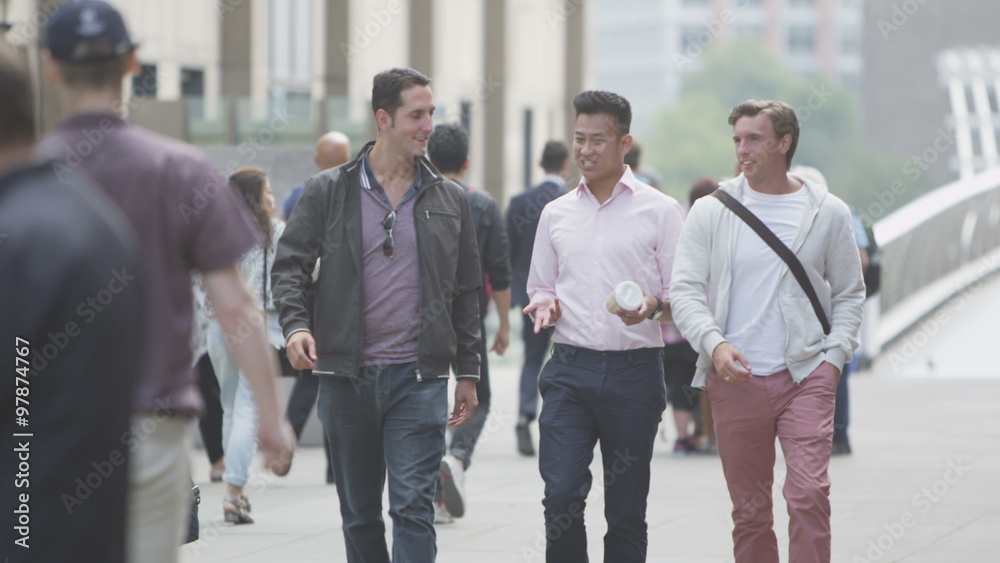 Happy casual male friends chatting as they walk through the city Happy casual male friends chatting as they walk through the city