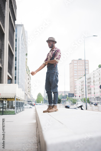 young handsome afro black man standing on a small wall, pulling