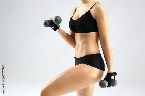 Sportowa kobieca sylwetka. Kobieta w stroju sportowym podnosi ciężarki.