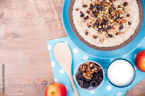 Breakfast set. A bowl of barley porridge with cocnut oil, vegetarian milk, walnuts, raisins, cinnamon on wooden background, polka dot napkins, spoon, apple, glass of vegetarian milk. photo