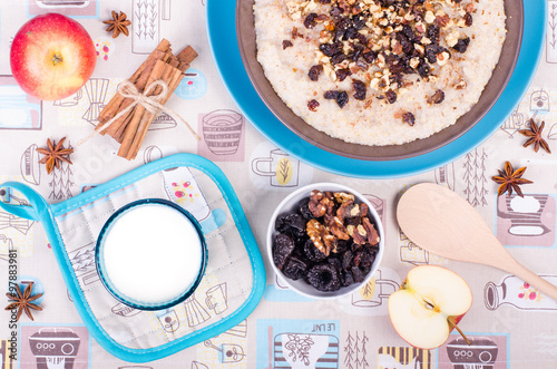 Breakfast set. A bowl of barley porridge with cocnut oil, vegetarian milk, walnuts, raisins, cinnamon on sackcloth, canvas, spoon, apple, glass of vegetarian milk. photo