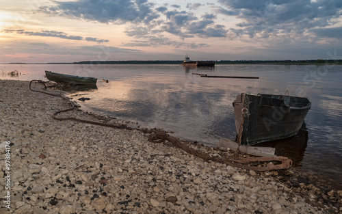 Two laid up wooden boats and cargo ship against Severnaya Dvina River panorama at sunset. Bereznik settlement, Arkangelsky region, Russia.
 photo