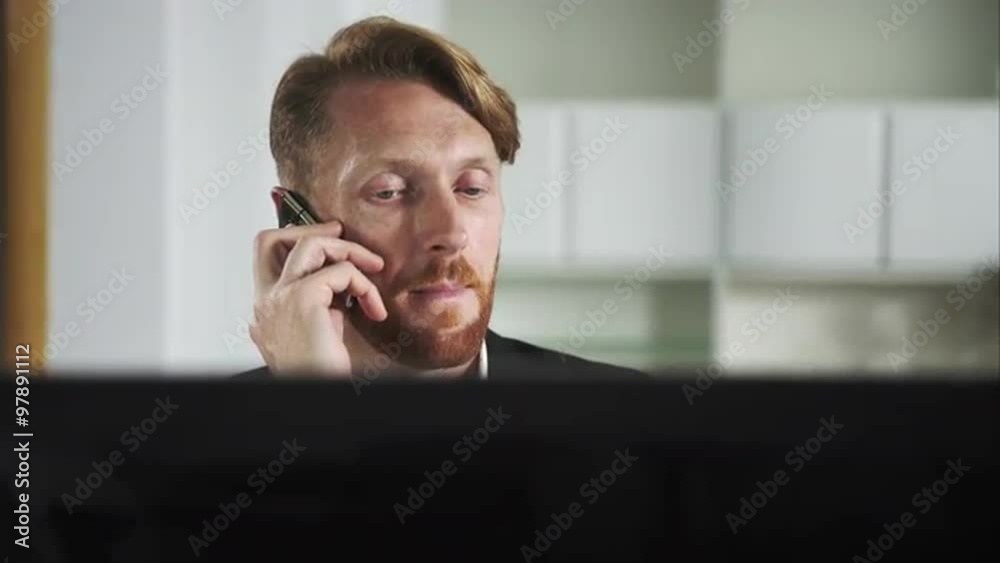 Red-haired man sitting at a computer and calling on the phone Red-haired man sitting at a computer and calling on the phone