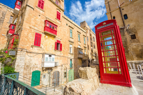 Old street of Valletta with red phone booth and traditional balconies and blue sky - Malta