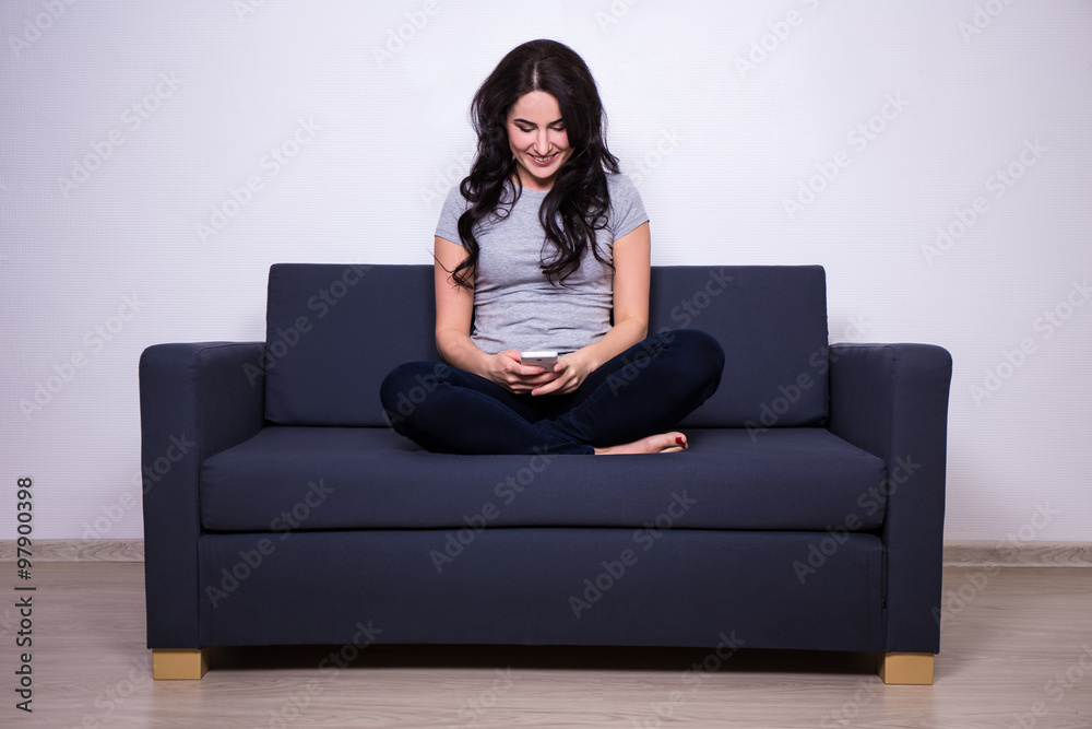 young happy woman sitting on sofa with mobile phone