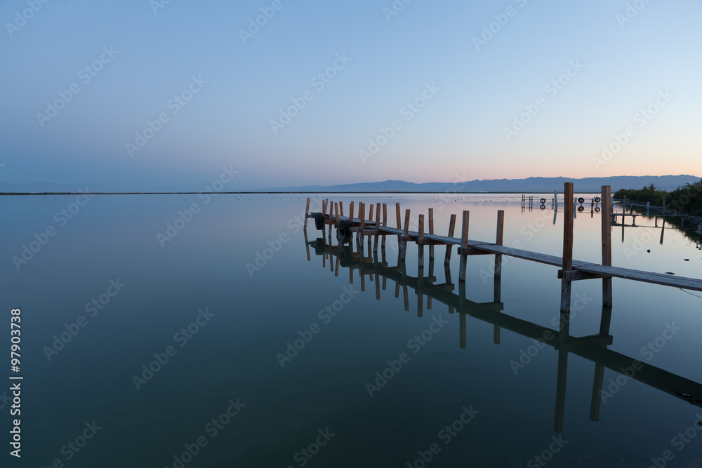 A calm sunrise by a wooden fishing pier.