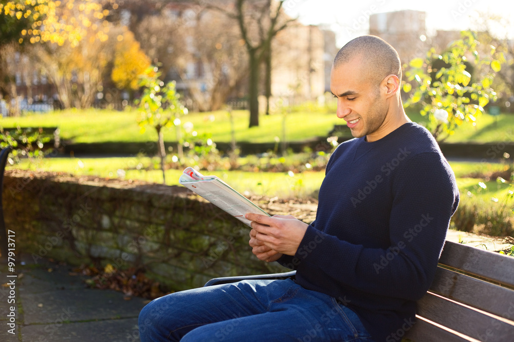 Young man sitting on a park bench reading a magazine Stock Photo ...