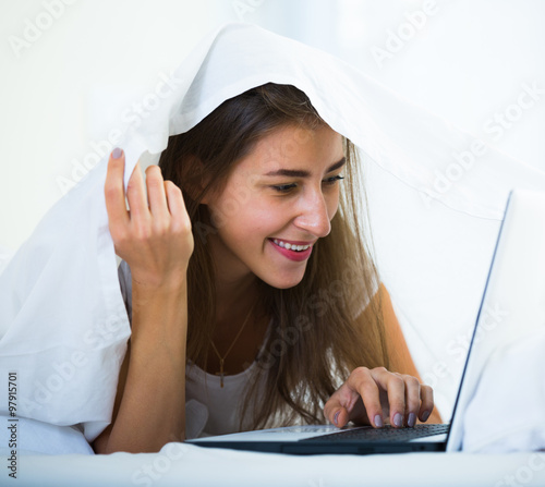 Teenage girl chatting online covered with blanket photo