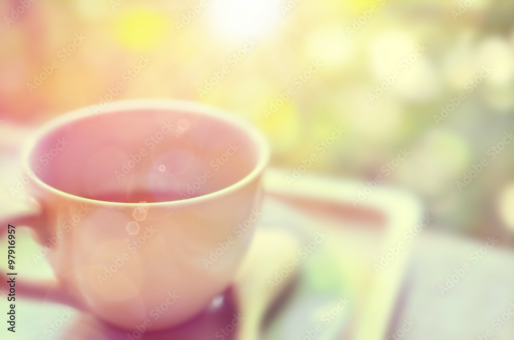 Fototapeta premium Blur a cup of coffee on wood table with green nature bokeh and morning sun light abstract background.