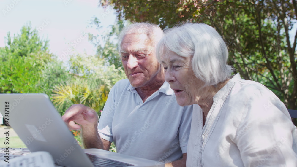 Cheerful senior couple having a skype conversation as they relax in the garden Cheerful senior couple having a skype conversation as they relax in the garden