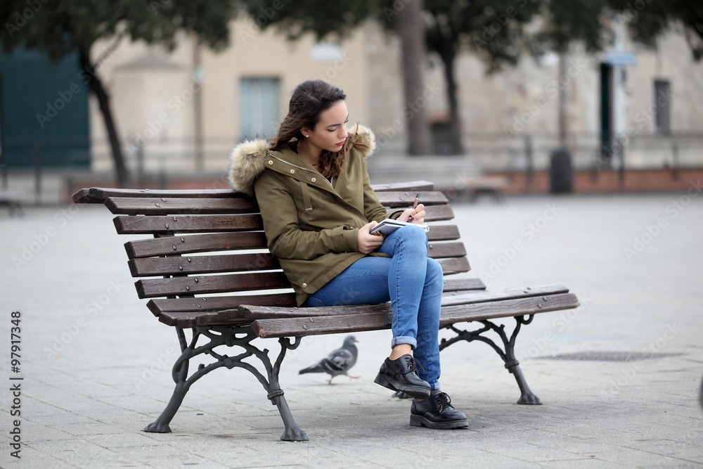 Young girl sitting on a bench writing in her diary Young girl sitting on a bench writing in her diary
