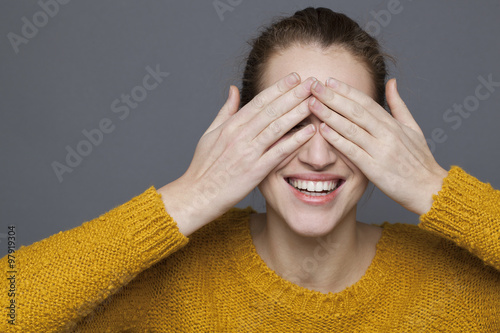 glowing happiness concept - cheerful 20s girl laughing in playing hide-and-seek for wellbeing and joy,studio shot on gray background
