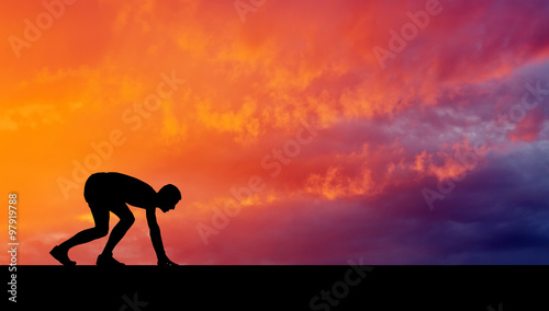 Silhouette of athlete in position to run on sunset background