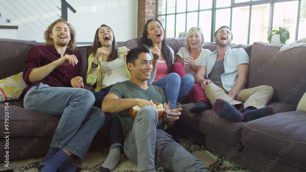 Group of attractive friends sit and eat popcorn whilst watching television. Group of attractive friends sit and eat popcorn whilst watching television.