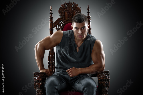 Muscular young man in a T-shirt and jeans, sitting on the throne.