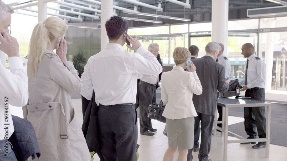 Business people on mobile phones as they wait in queue at airline security Business people on mobile phones as they wait in queue at airline security