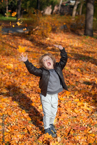 Happy little boy throwing leaves in the air in autumn park and having fun. © FotoCuisinette