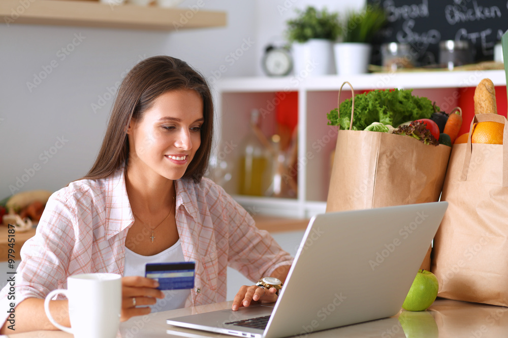 Smiling woman online shopping using tablet and credit card in kitchen Smiling woman online shopping using tablet and credit card in kitchen