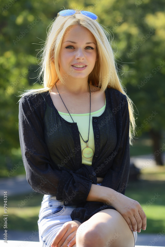 Blond teenager sitting on stone in park and looking at camera Blond teenager sitting on stone in park and looking at camera