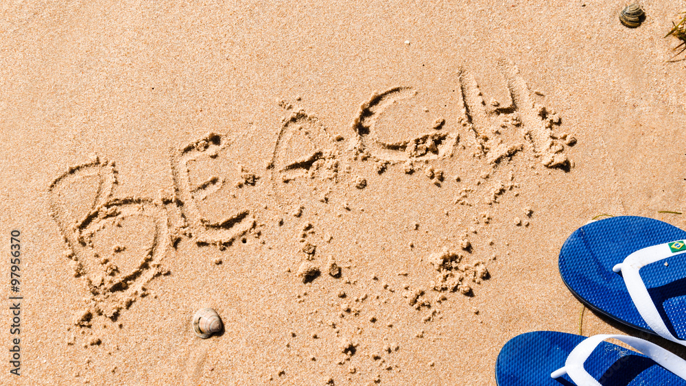 the word beach wrote on the sand with a shell and blue flip-flops