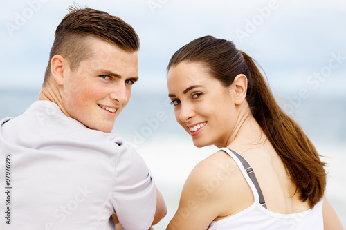 Young couple looking at camera while sitting next to each other on beach © Sergey Nivens