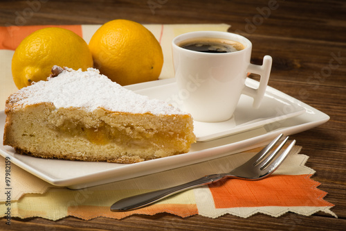 A piece of lemon pie and a cup of tea on the wooden background.