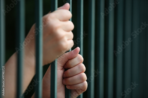Two hands clutching prison bars