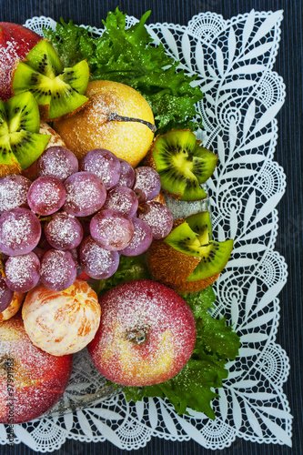 Fruits sprinkled with powdered sugar on a plate on a blue background