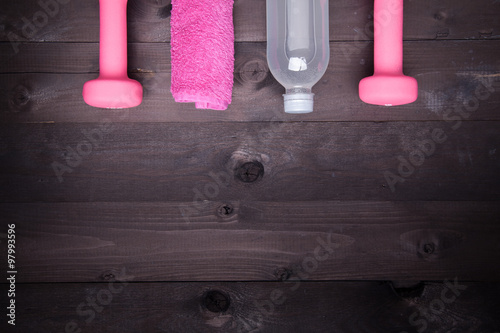 Sport equipment. Water bottle, pink towel and a  pink dumbbell on a black wooden background photo