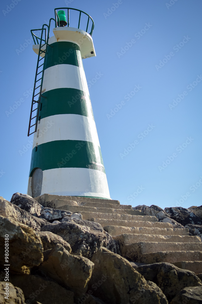 Beautiful lighthouse with bright sun on top on sky background