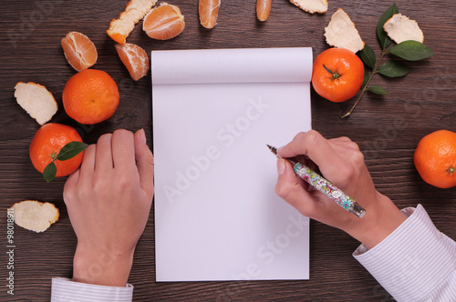 Winter Time  and Christmas background. Mandarins and blank paper on wooden background, copy space image Close up on female hands writing wish list for new year, woman writing  new year goals photo