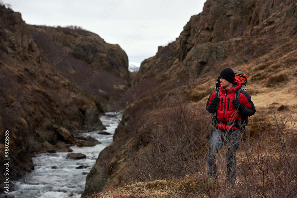 Man treks along river with backpack
