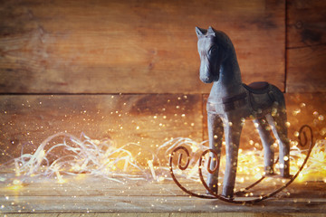double exposure image of rocking horse and magic christmas lights on wooden table