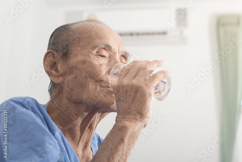 Old man holds and drinks glass of water