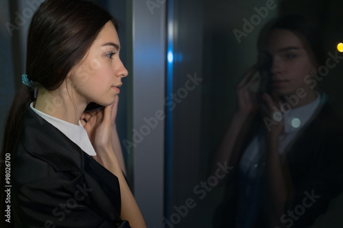 Businesswoman with cellphone looking out the window late at night