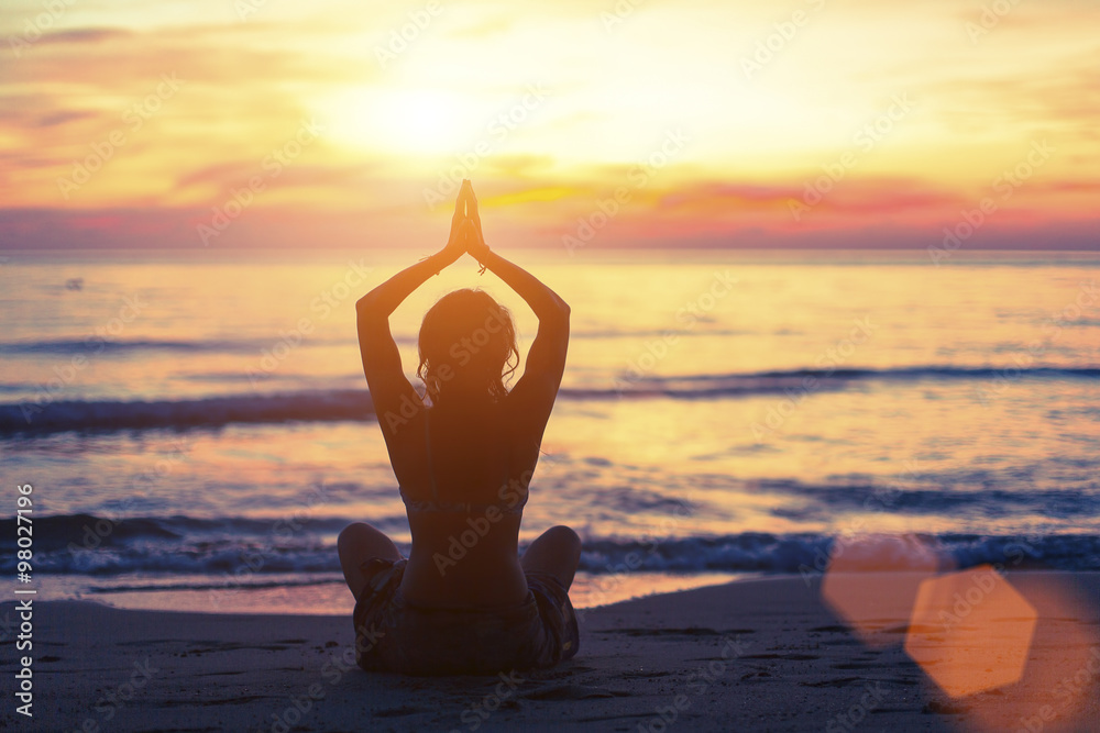 Silhouette of young girl in yoga pose sitting on the beach during ...