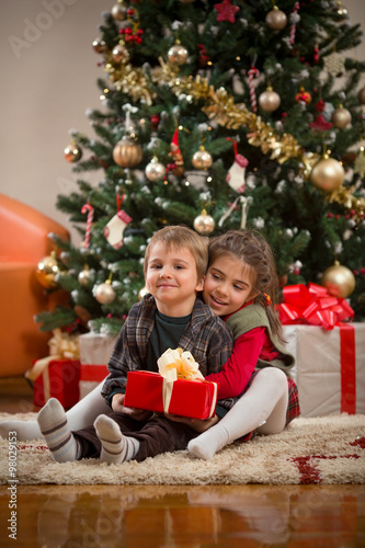 Cute little girl embracing her little brother while opening Christmas presents