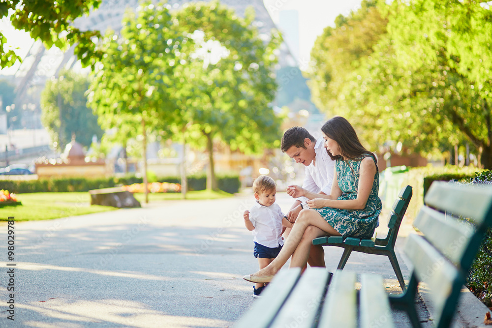 Happy family of three sitting on the bench near the Eiffel tower Happy family of three sitting on the bench near the Eiffel tower