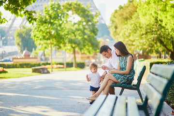 Happy family of three sitting on the bench near the Eiffel tower