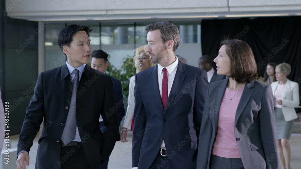 Large diverse business group talking as they walk through office building Large diverse business group talking as they walk through office building