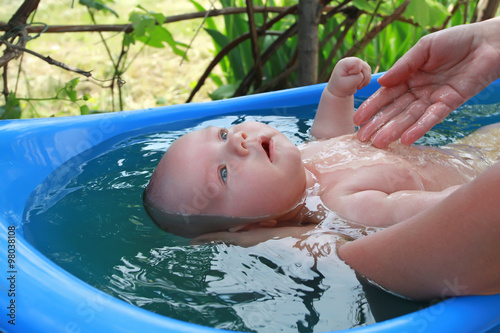 Mum bathes baby in a blue bath. Bathing the baby in the vineyard