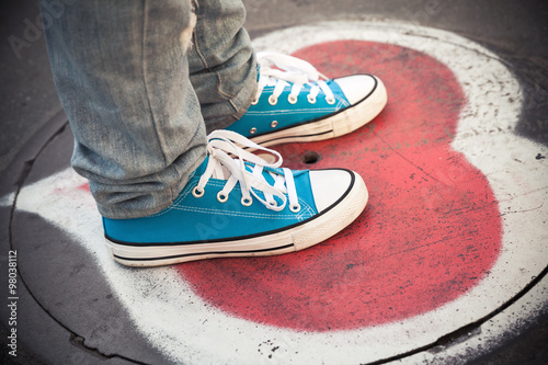 Blue sneakers, teenager feet standing on sewer manhole