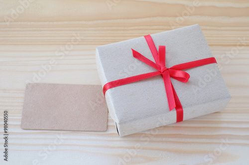 Vintage gift box with red ribbon bow and card on wood background