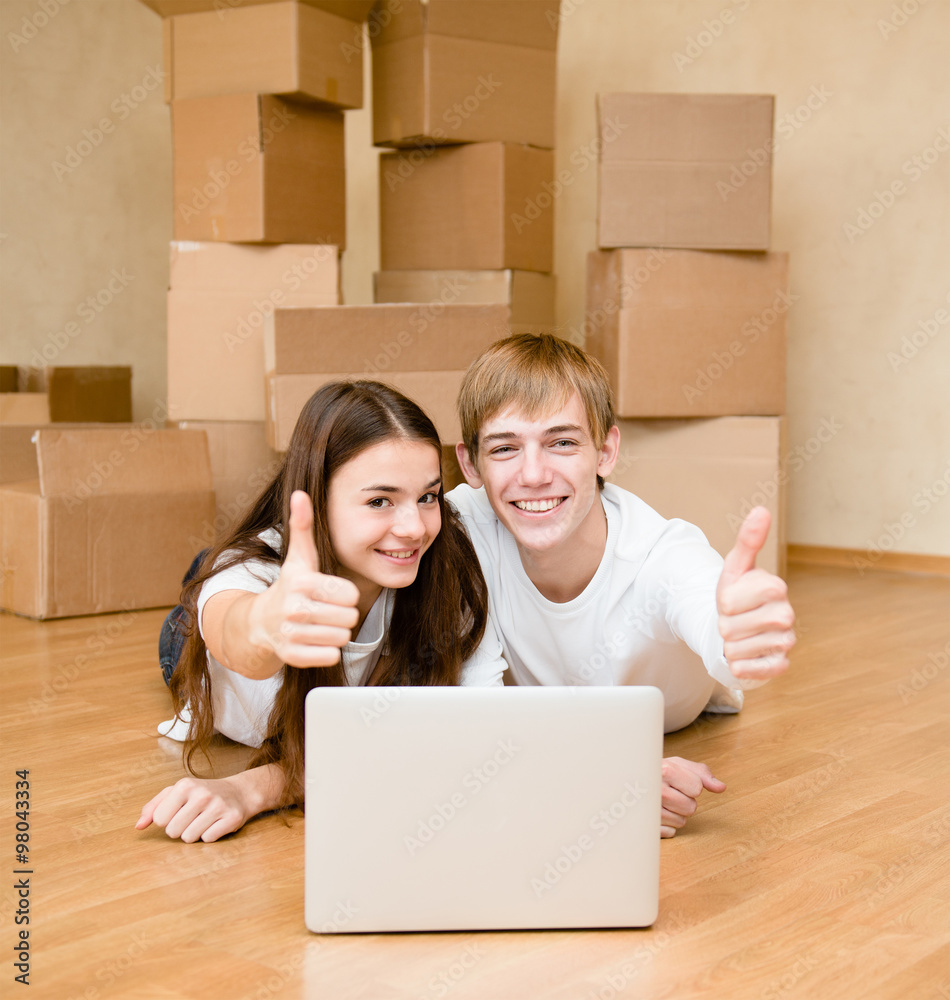 young couple using laptop in their new home and showing thumbs u young couple using laptop in their new home and showing thumbs u