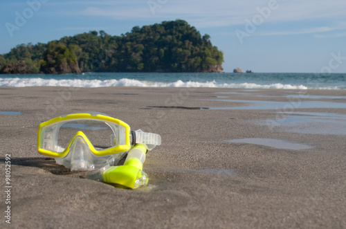 Yellow Scuba Mask and Snorkel (off center) on a beach in Costa Rica. Part of Manuel Antonio Rainforest in background.
