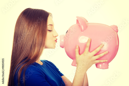 Teenage woman kissing piggybank.