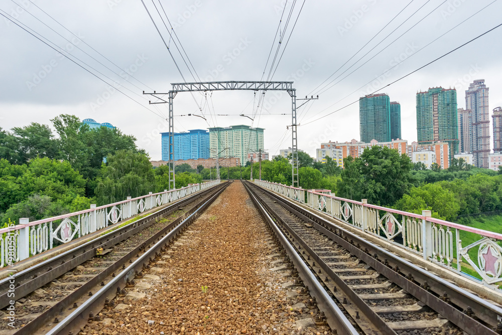 Straight railroad on bridge vanishing in horizon with power line against skyline background. Moscow, Russia. 

