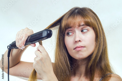 The young woman straightens hair the curling iron