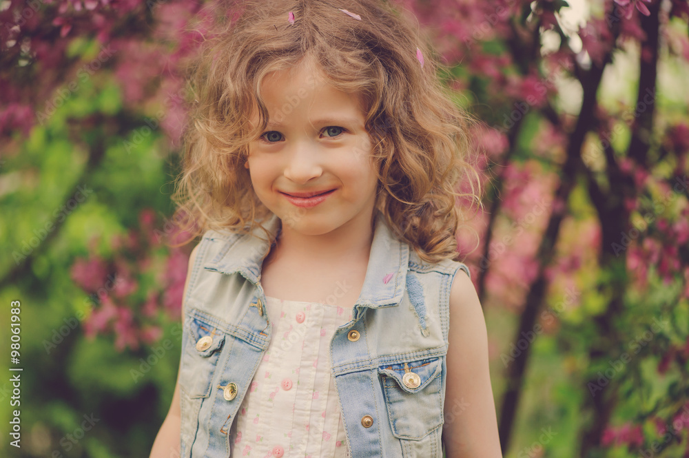 cute child girl in jeans vest enjoying spring near blooming crab apple tree in country garden